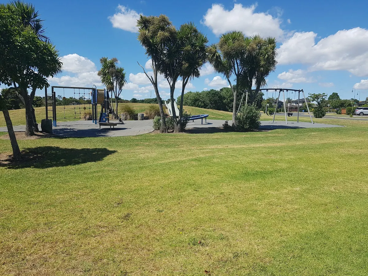 Multi-play slide and swings on a sunny lawn at Wattle Downs Esplanade Reserve playground, Auckland