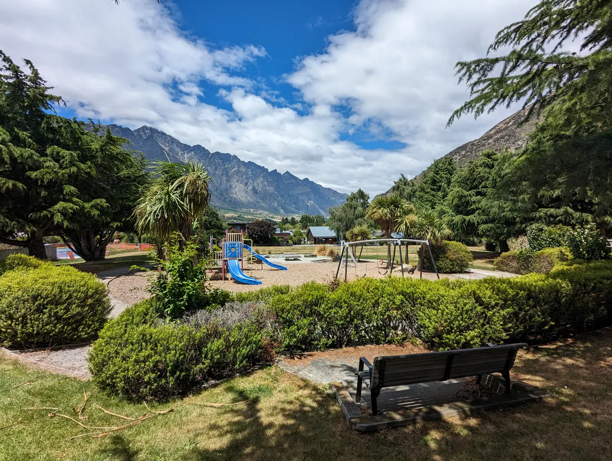 Blue slides and swing frame at Kawarau Falls playground with mountains behind, Frankton