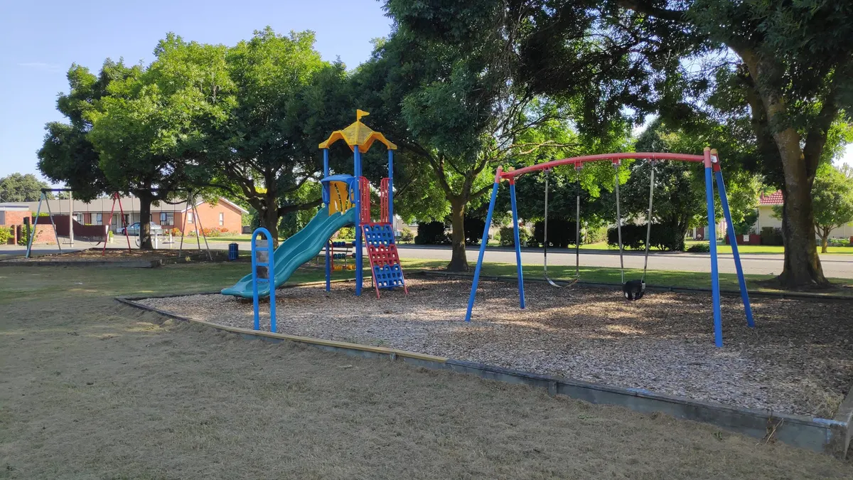 Slide tower and swing set on bark beside lawn at Mona Square playground, Ashburton