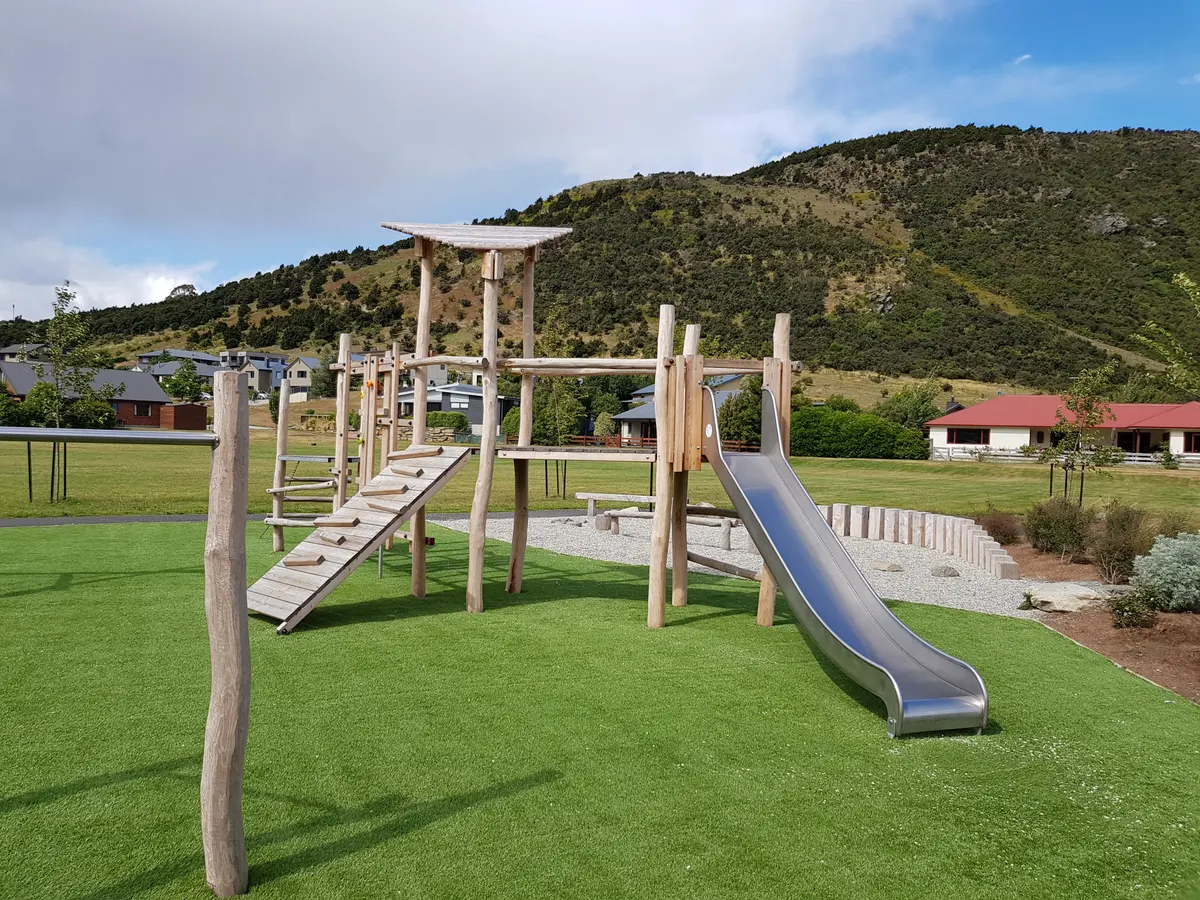 Timber climbing frame with metal slide on soft turf at Allenby Park playground, Wānaka