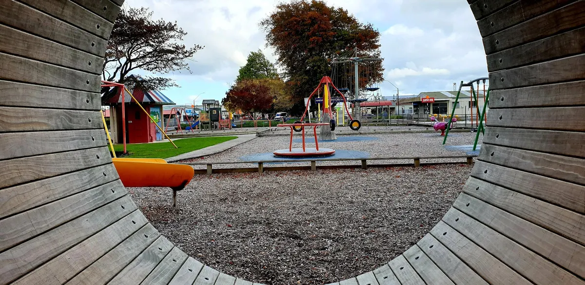 Roundabout, swings and slides seen through a wooden tunnel at Harvard Adventure Park, Pahiatua