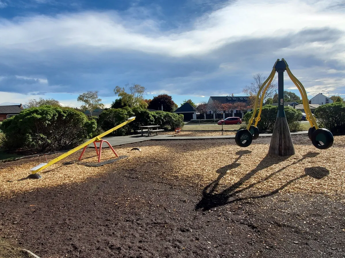 Yellow see-saw and tyre swing ride on bark chip at Ray Blank Park playground, Ilam