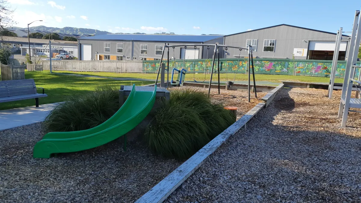 Green slide, swings and climbing frame on bark at Hukatai Park playground, Elsdon