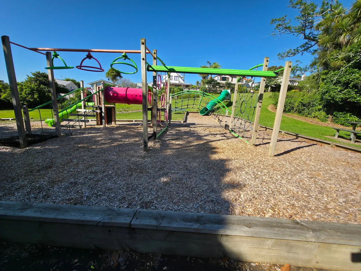 Net climber, pink tunnel and green slides over bark at Konini Playground, Greenlane