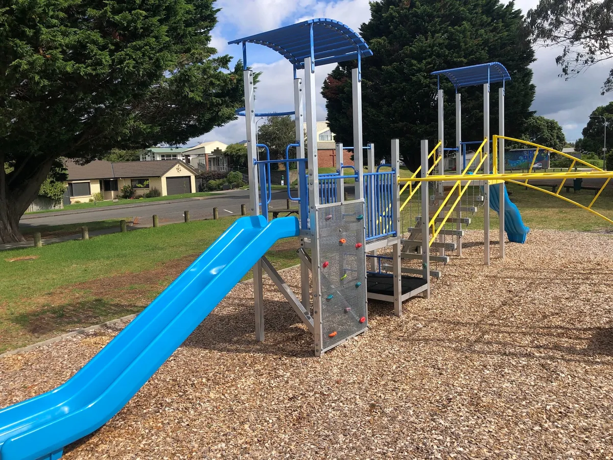 Climbing wall, tower and long blue slide on wood chip at Weka Park playground, Raumati Beach