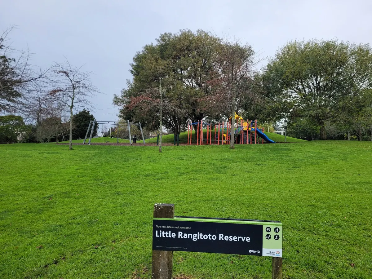 Climbing frame and swings on a grassy rise behind the Little Rangitoto Reserve sign, Remuera