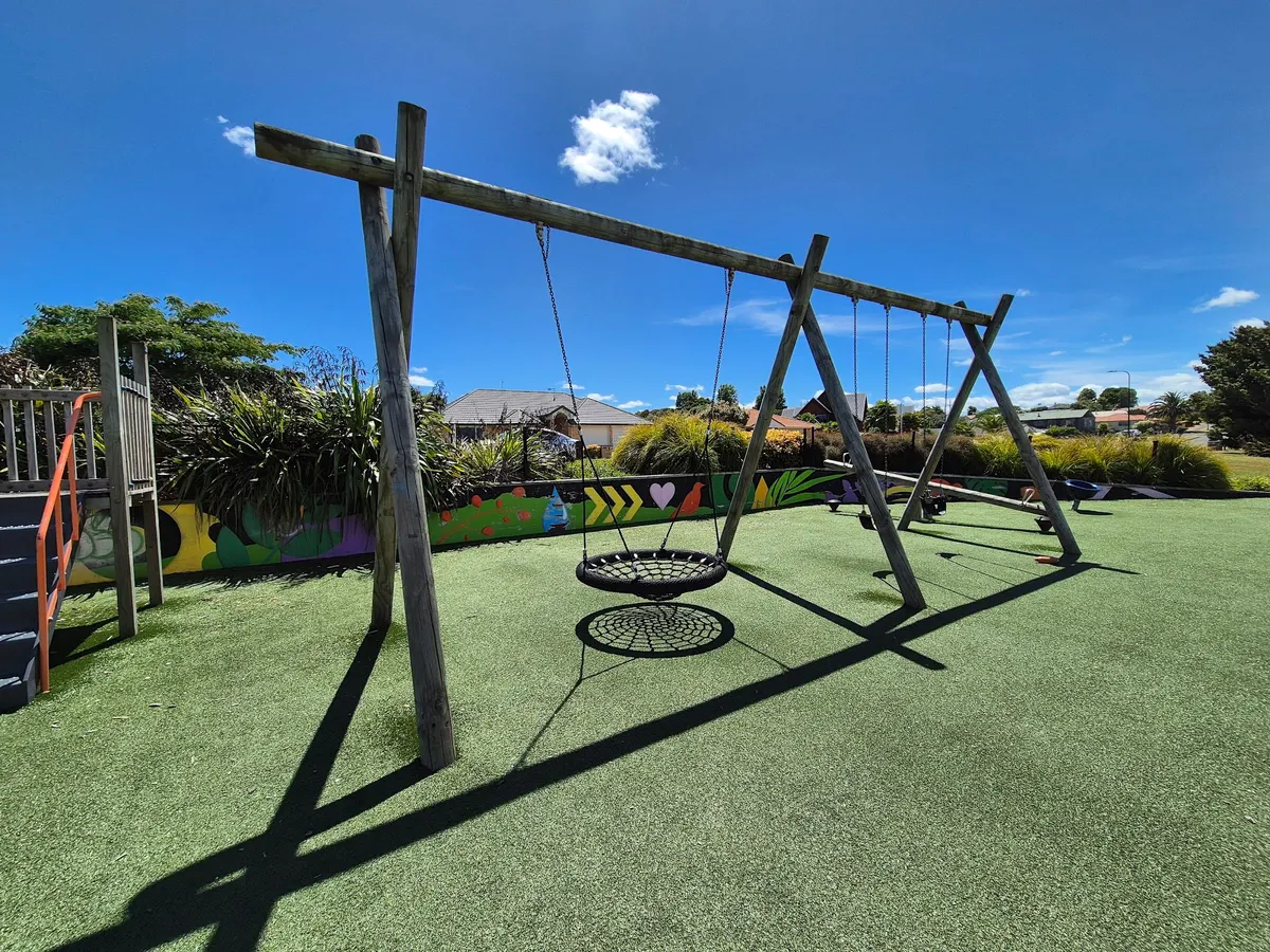 Nest swing and junior climbing unit on artificial grass at Te Kootii Park playground, Hamilton
