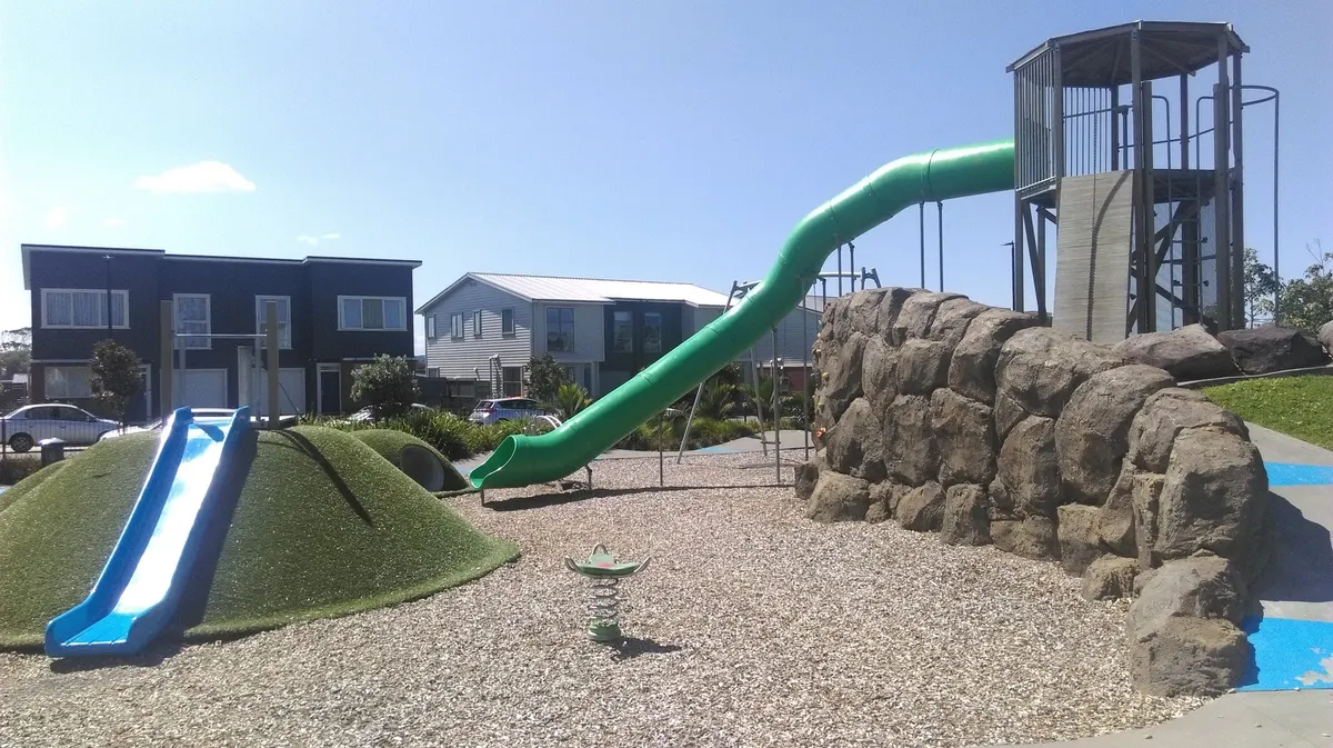 Green tunnel slide, rock-wall tower and turf mound slide at Whenuapai Settlement Playground, Auckland