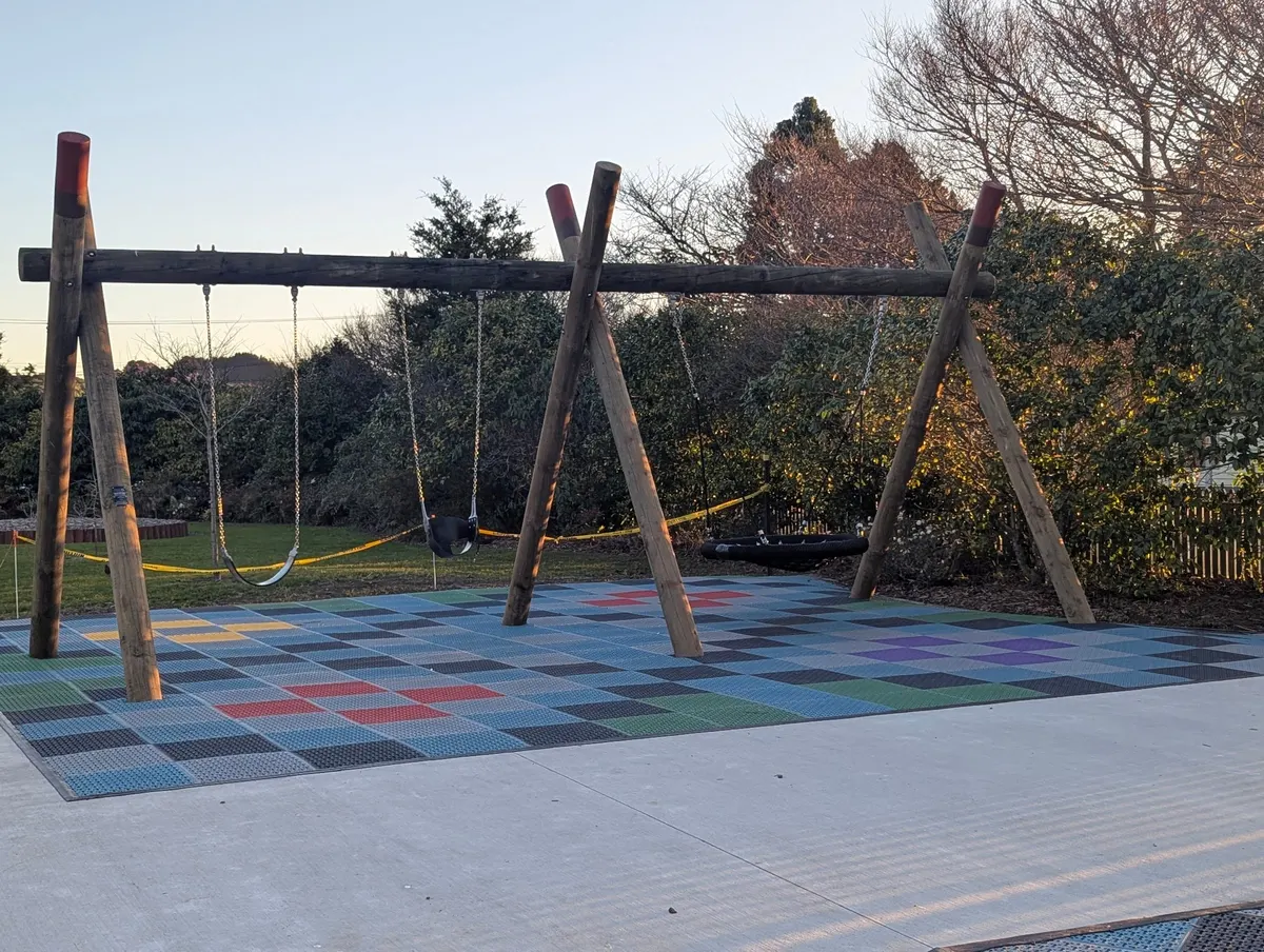 Timber swing frame on coloured interlocking tiles at Elizabeth Rose Park playground, Waikanae