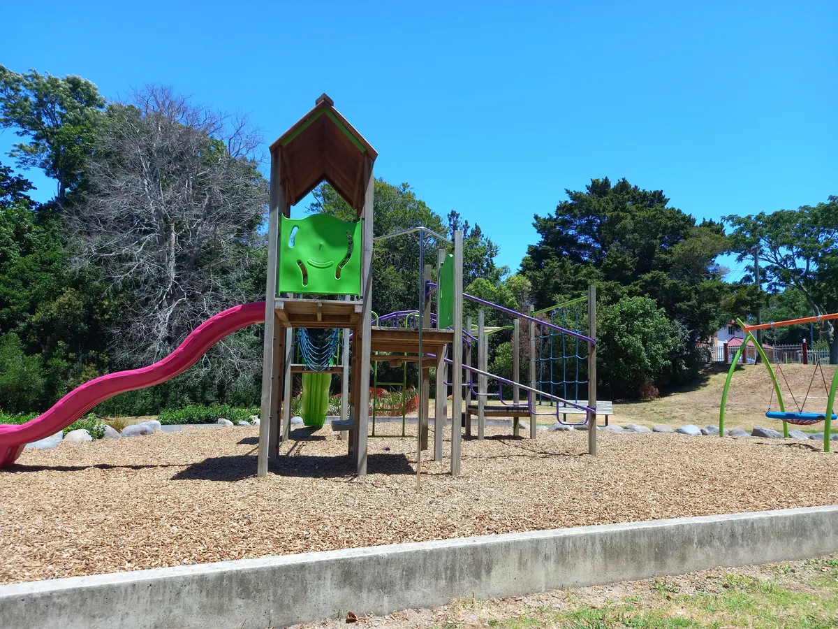 Wooden play tower with pink slide and rope bridge on bark at Fowlds Park playground, Mount Albert