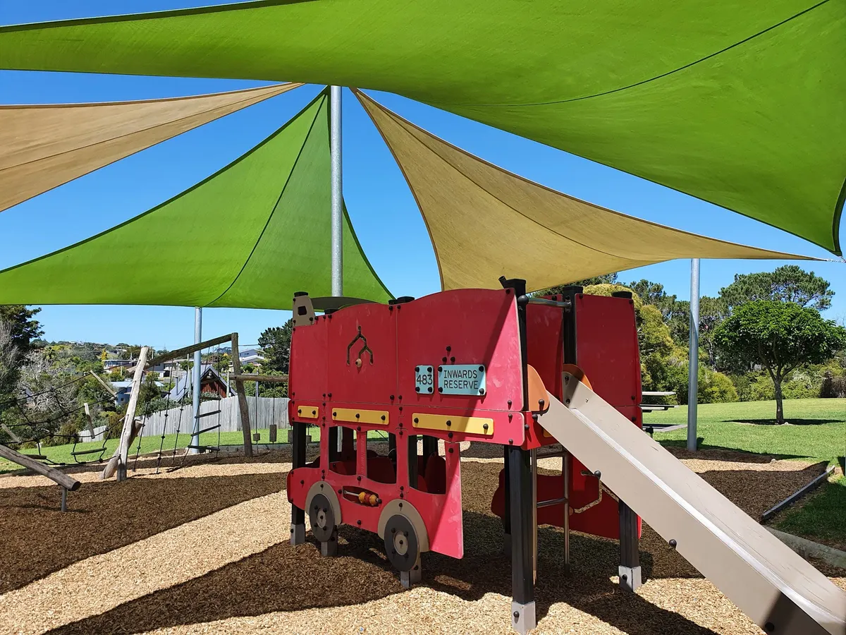 Red play bus and slide under green and sand shade sails at Inwards Reserve playground, Birkdale