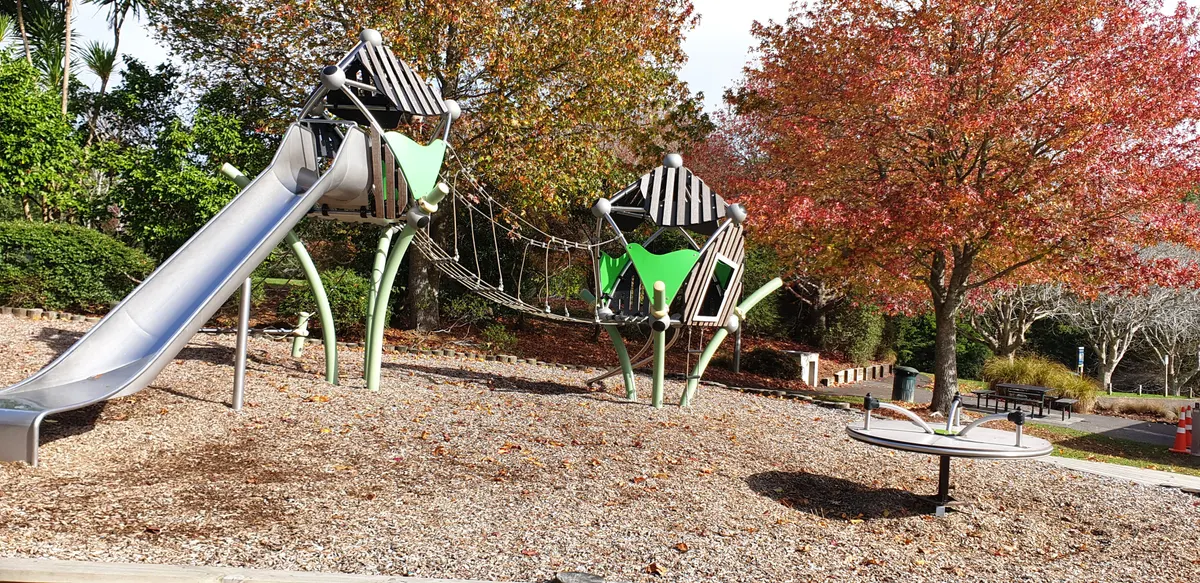 Silver slide, rope bridge and carousel on bark among autumn trees at Children Playground, Terry Street, Blockhouse Bay
