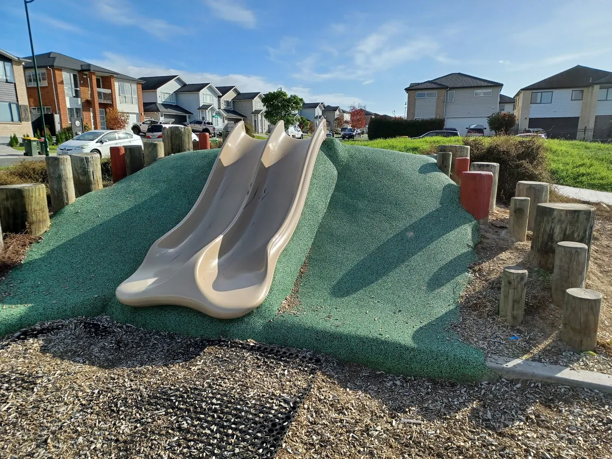 Twin slides on a green rubber mound with log posts at Hughs Way Playground, Flat Bush