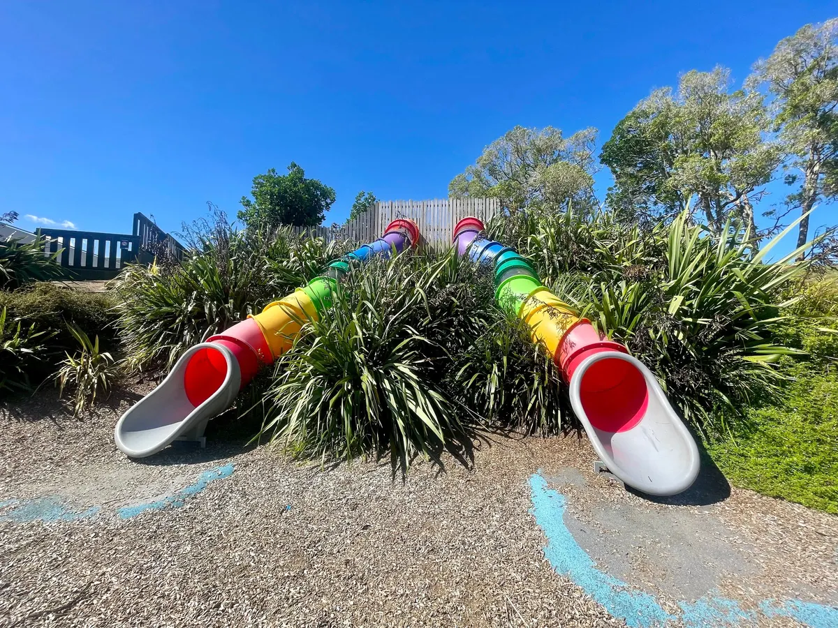 Two rainbow tube slides running down the bank at Aronia Park playground, Goodwood Heights
