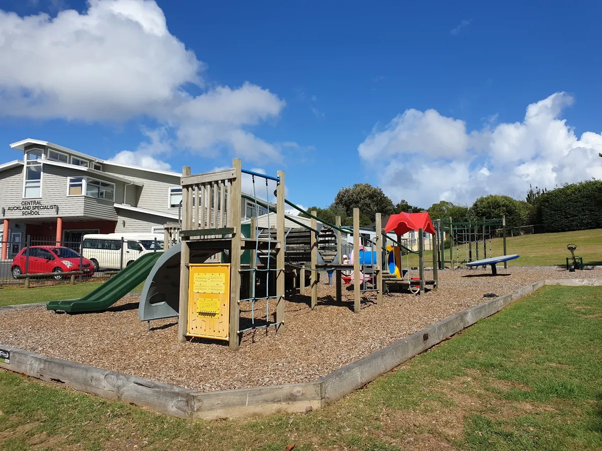 Wooden play tower with green slide and seesaw on woodchip at Smallfield Reserve Playground, Mount Roskill