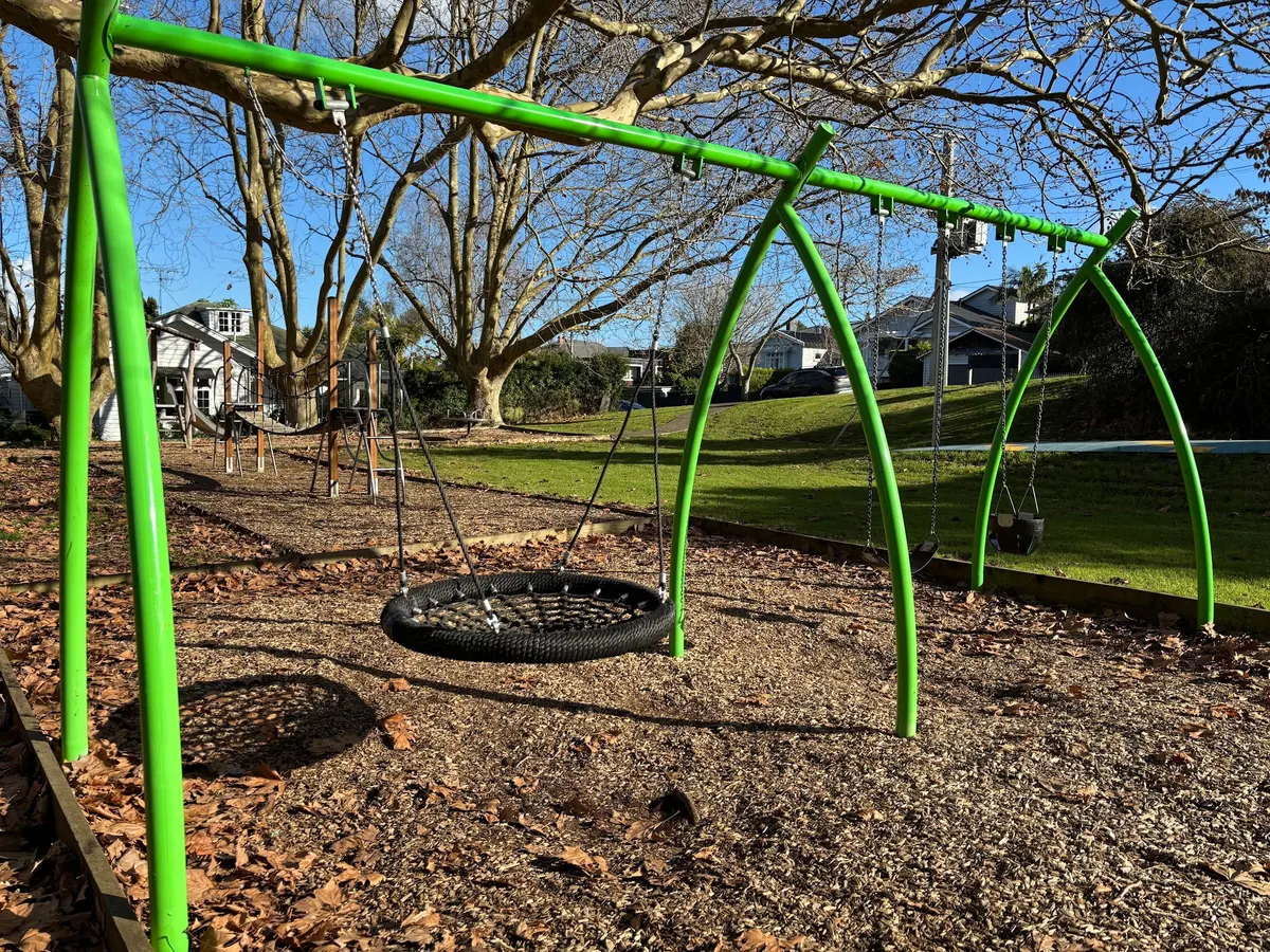 Green basket swing frame under big trees at Wairua Reserve playground, Remuera