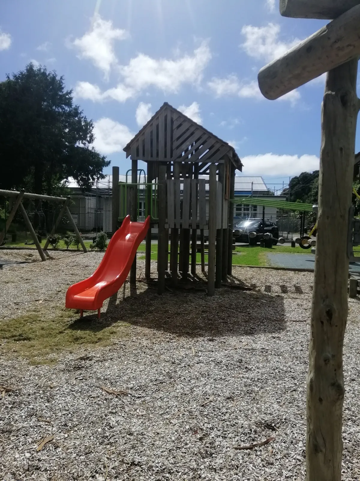 Wooden play tower with orange slide and swing frame on bark at Tennis Court Road Playground, Raumati South