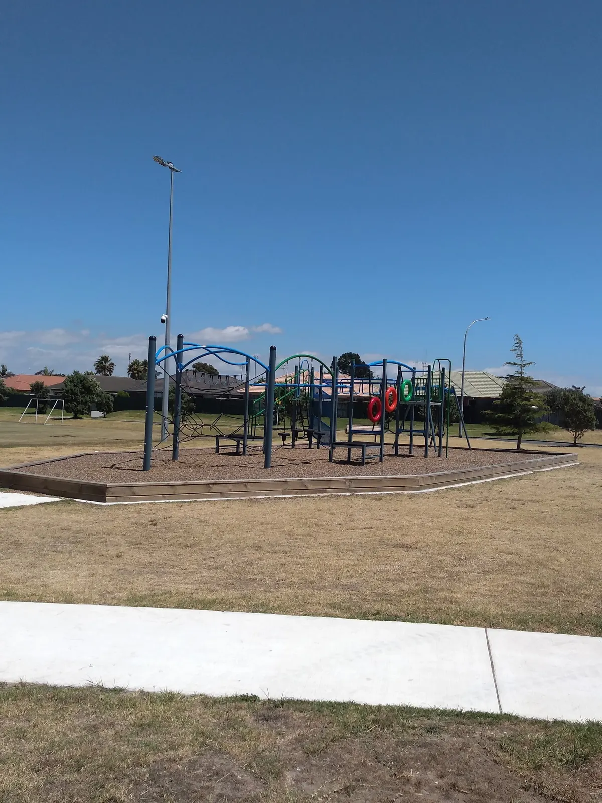 Blue multi-play tower with red and green rings on a bark pad at Oceandowns Reserve playground, Mount Maunganui