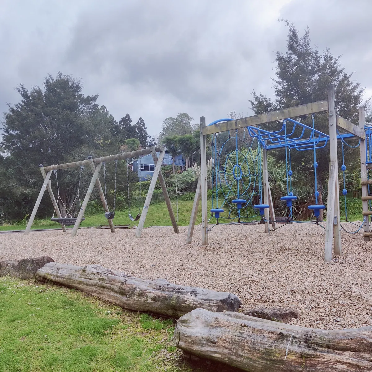 Swing set and rope climbing frame on bark at Whau Valley Parklands playground, Te Kamo