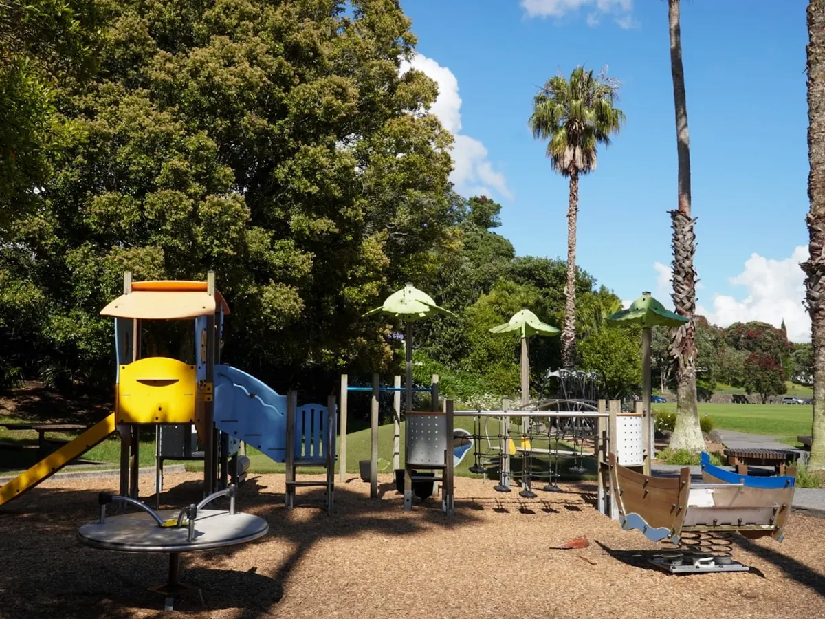 Slides, spinner and boat rocker on bark under trees at Grey Lynn Park playground, Auckland