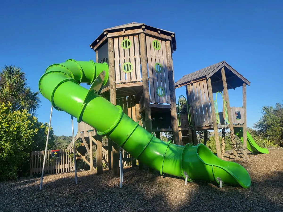 Green tubular slide and timber tower at Waikōwhai Park playground, Hillsborough
