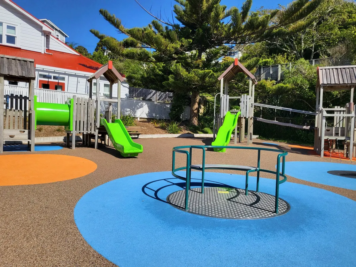 Inclusive carousel, timber play towers and green slides at Wadestown play area, Wellington