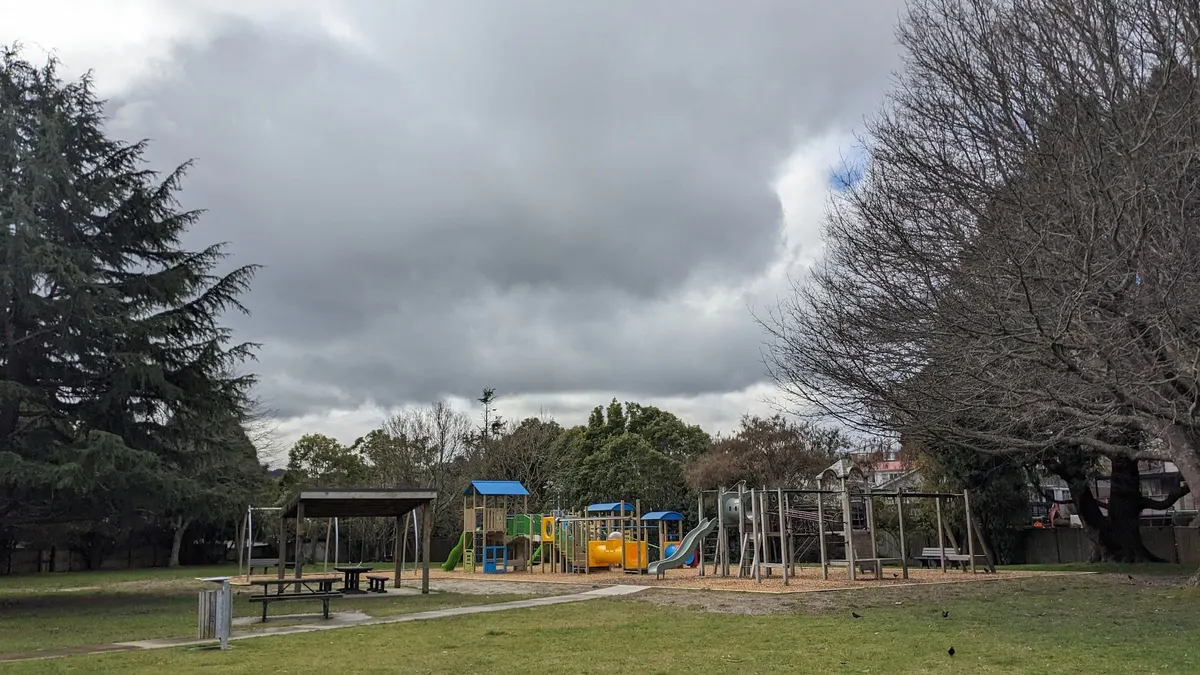 Colourful play structure and older timber gear across the grass at Silverstream Park playground, Upper Hutt