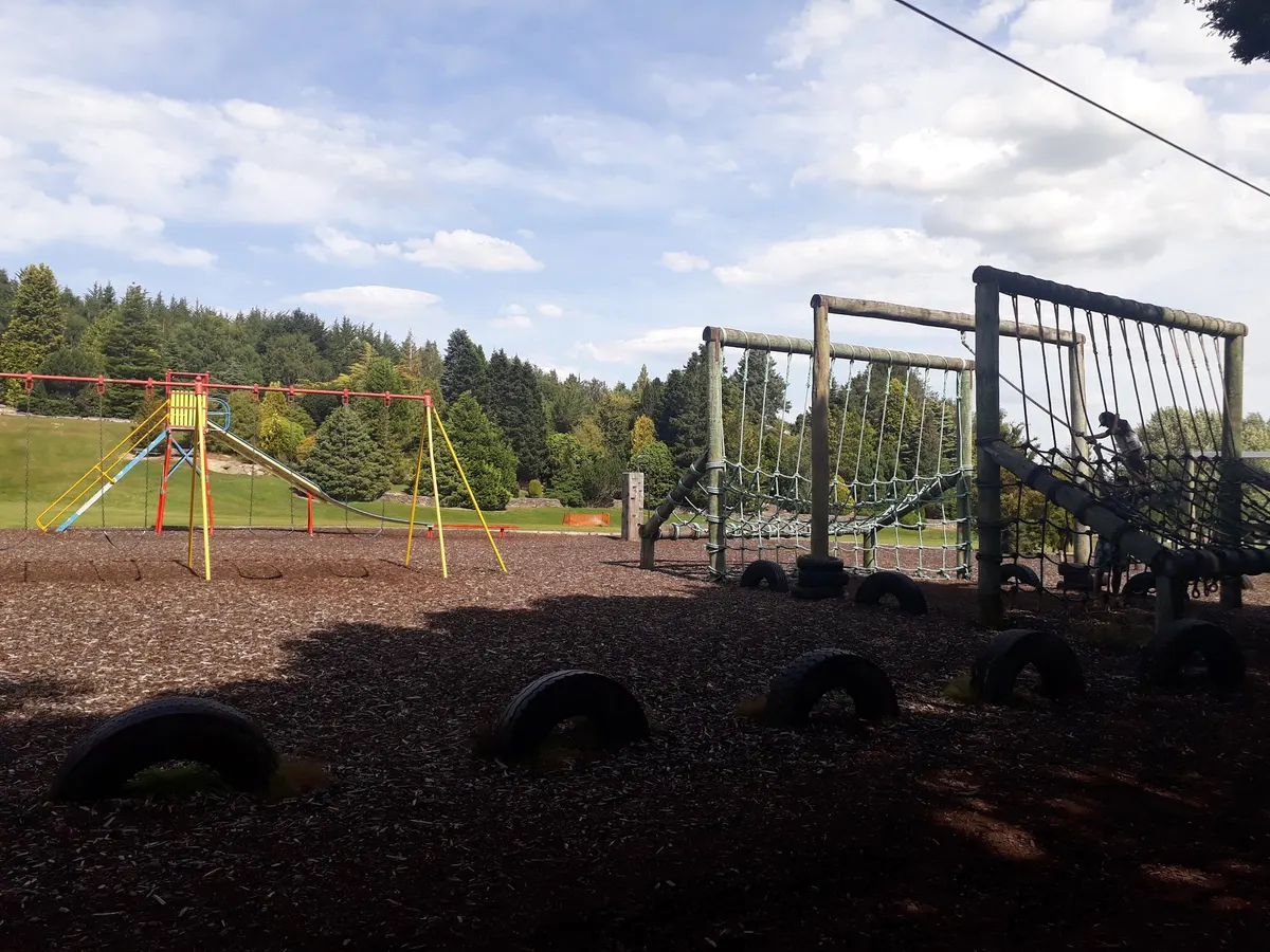 Rope cargo-net frames, tyres and a slide frame on a bark play area at Dolamore Park playground, Gore