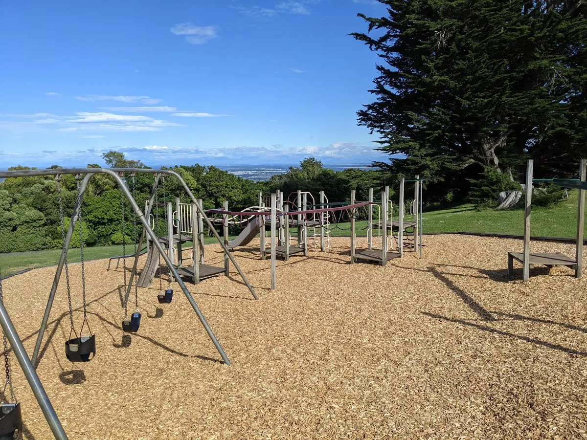 Swings and multi-play structures on woodchip with Canterbury views at Victoria Park playground, Cashmere