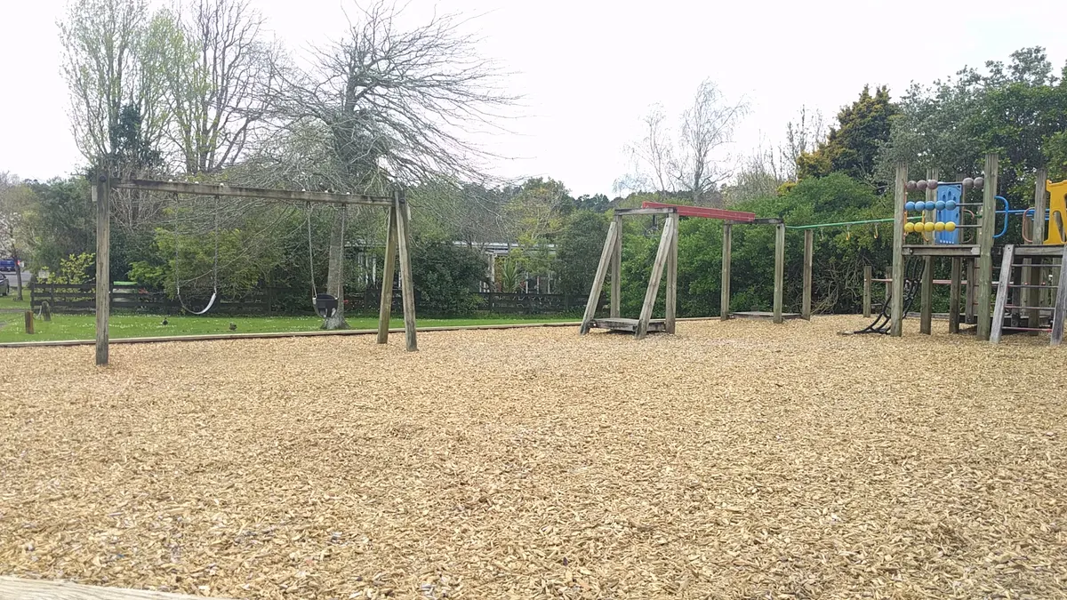 Swings and timber climbing frame on woodchip at Robert Knox Memorial Park, Swanson