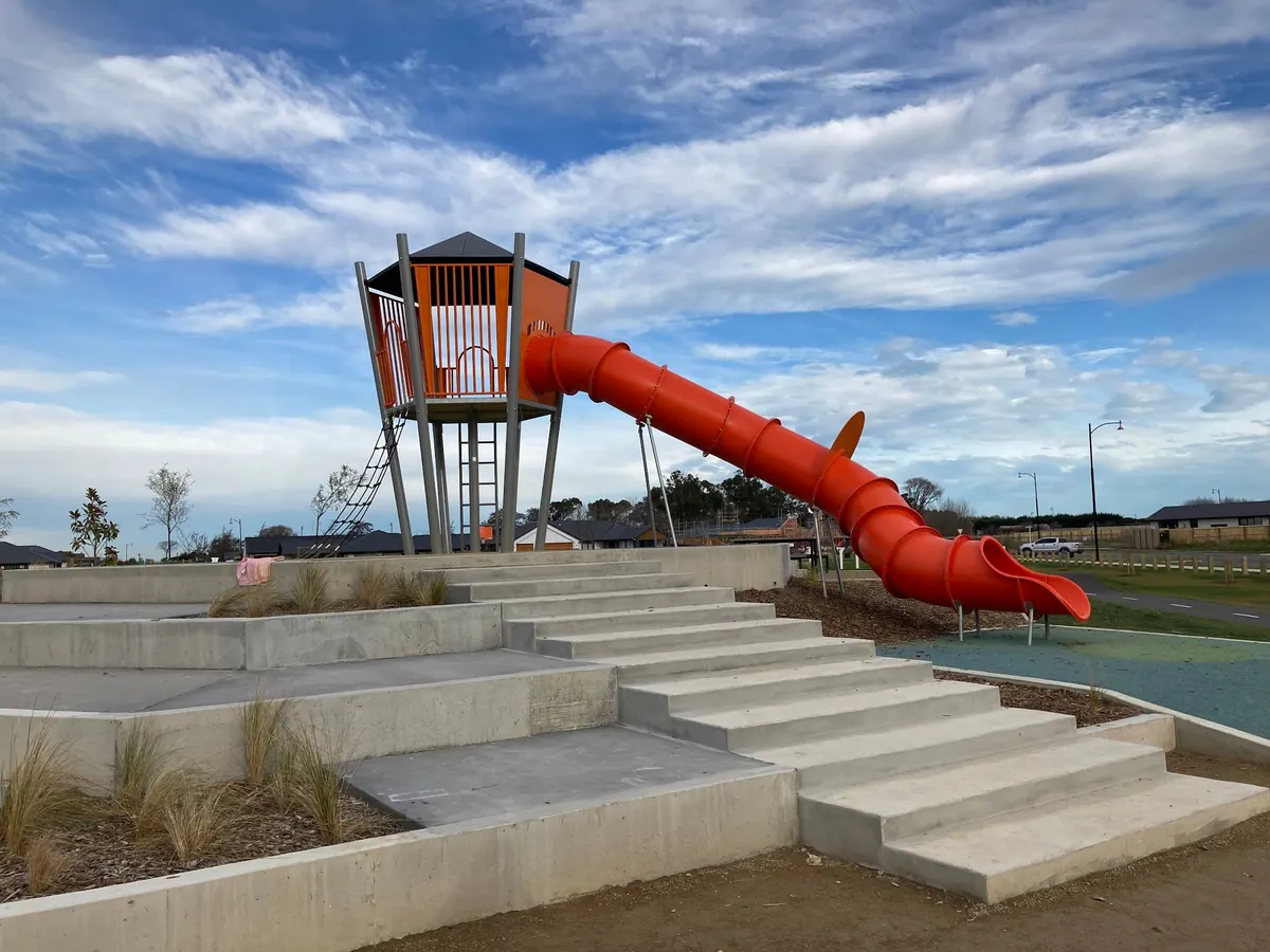 Orange tower and tube slide above concrete terraces at Te Whariki Playground, Lincoln